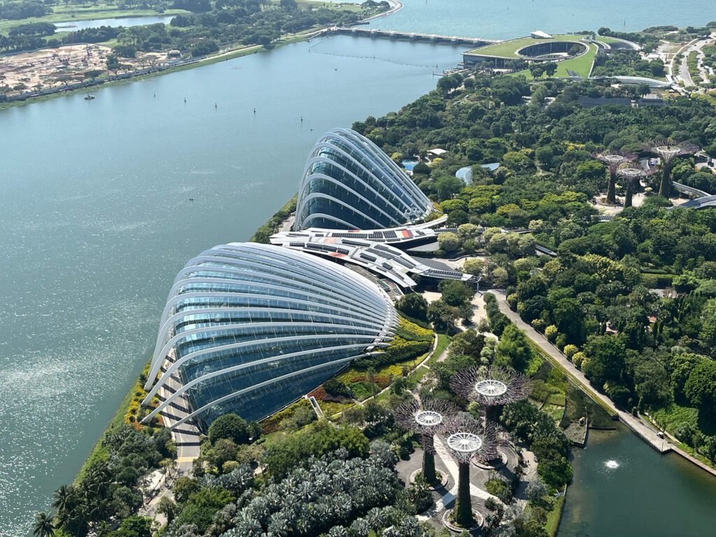 Shell-like glass and steel domes dominate the riverside landscape, along with the Supertrees, at Gardens by the Bay in Singapore. In the foreground is the Flower Dome, with the Cloud Forest Dome behind.