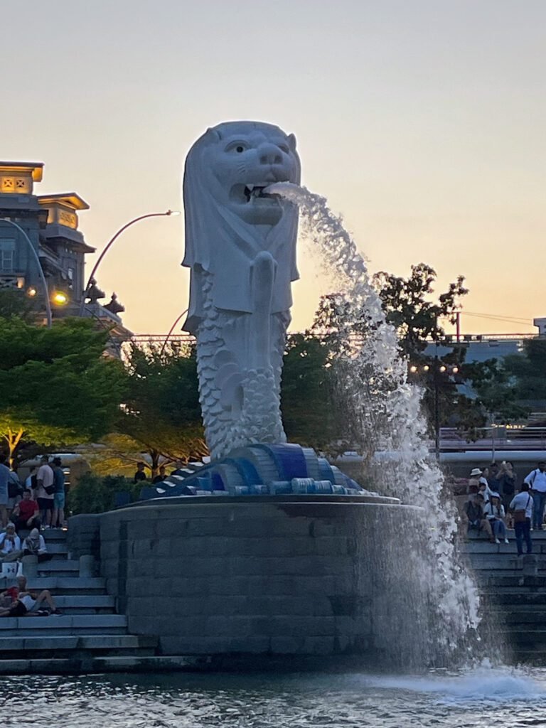 The Merlion stands guard at the river's edge, half-lion, half-fish, looking both mystical and majestic in the twilight.